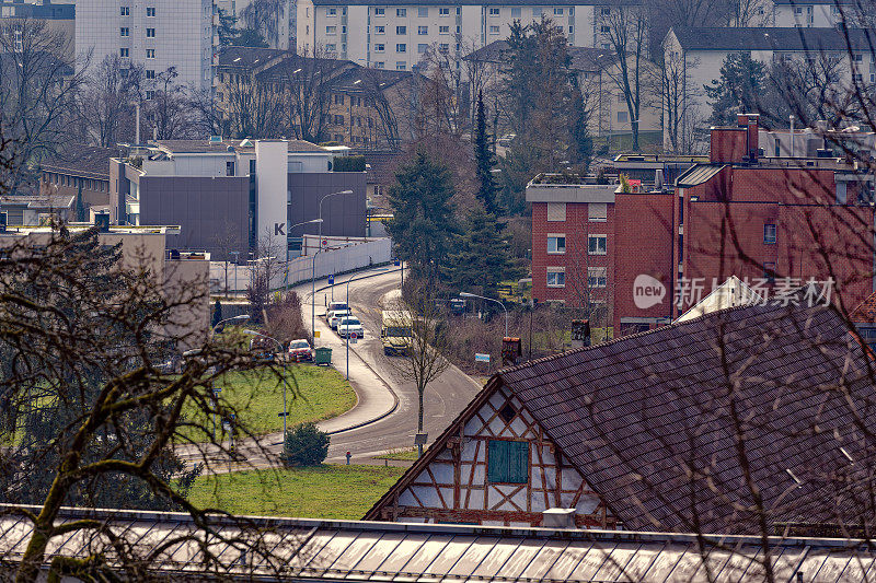 Modern red apartment buildings with old half-timbered farm house in the foreground at City of Zürich with winding road on a sunny winter noon.